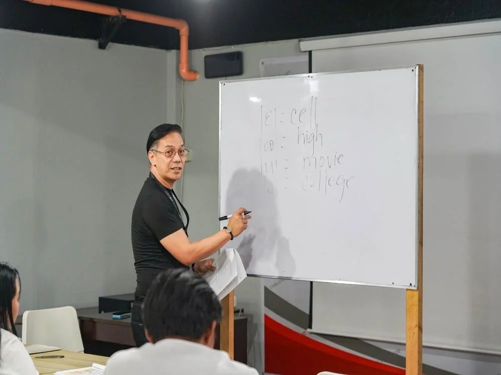 教室で男性講師がホワイトボードを使って生徒たちに何かを教えている様子