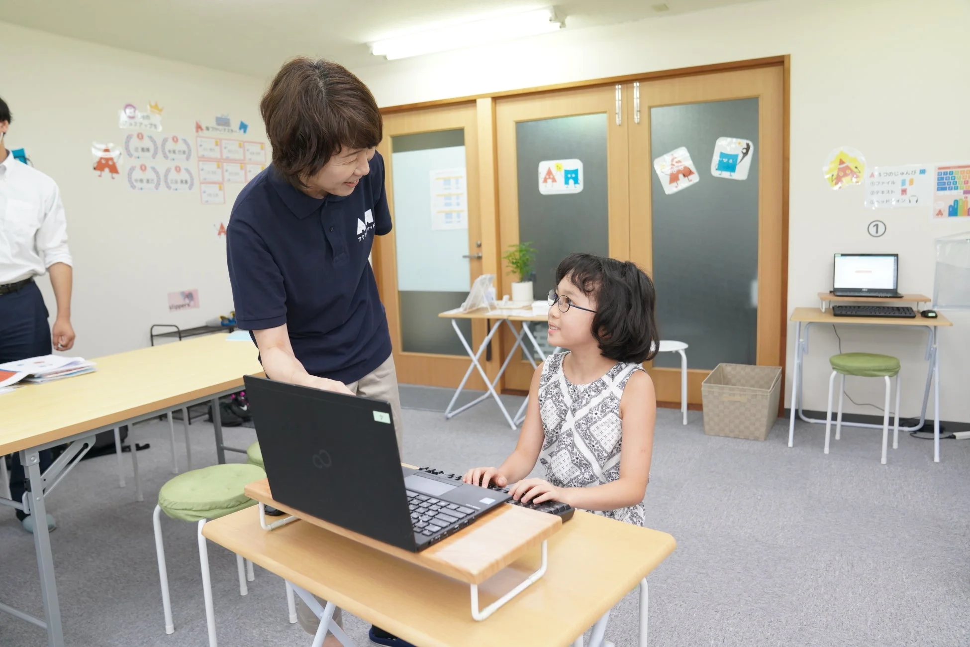 教室で指導者が少女にパソコンを教えている様子