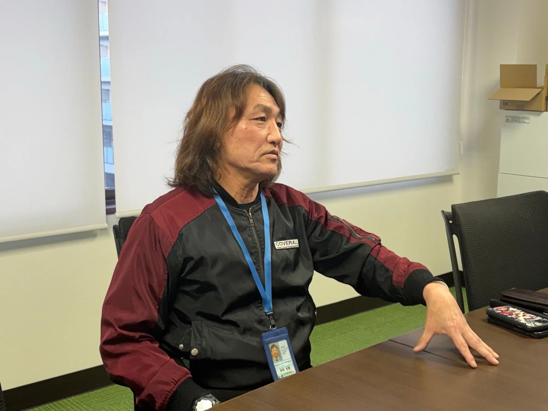 長髪の男性が会議室で真剣な表情で座っている様子