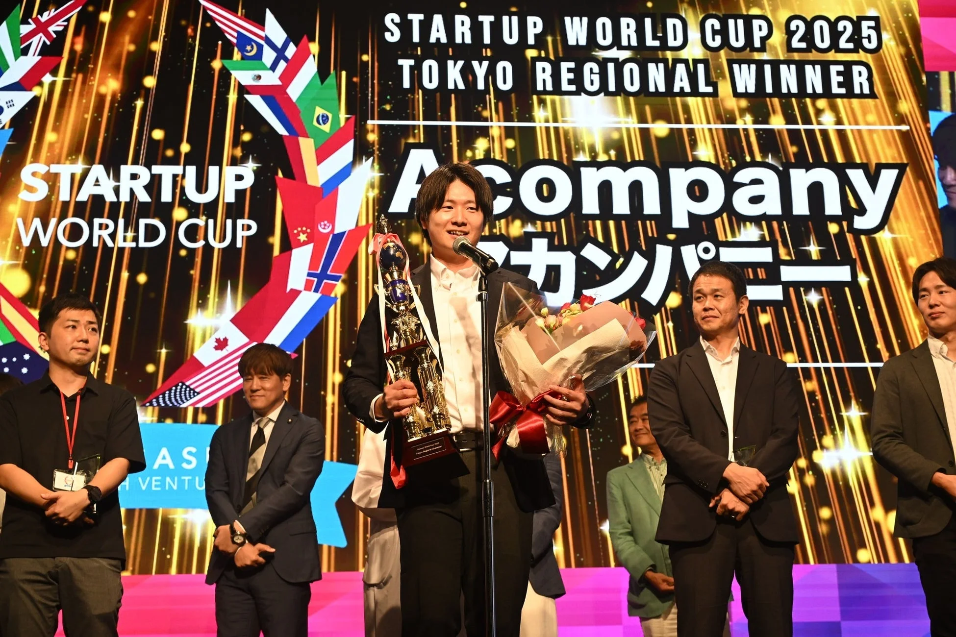 STARTUP WORLD CUP 2025 東京地域大会の優勝者がトロフィーと花束を手にスピーチしている場面