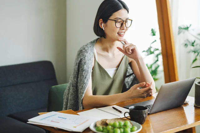 自宅でノートパソコンに向かい、リラックスした雰囲気で仕事やオンライン会議をしている若い女性の様子。