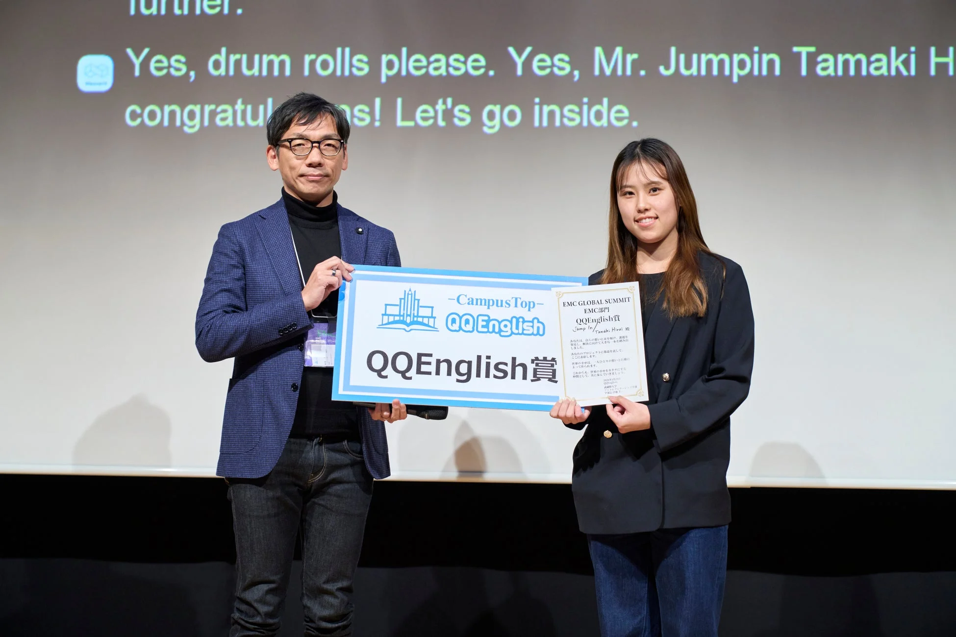 「QQEnglish賞」の表彰式で、賞状と看板を手に笑顔の受賞者と関係者