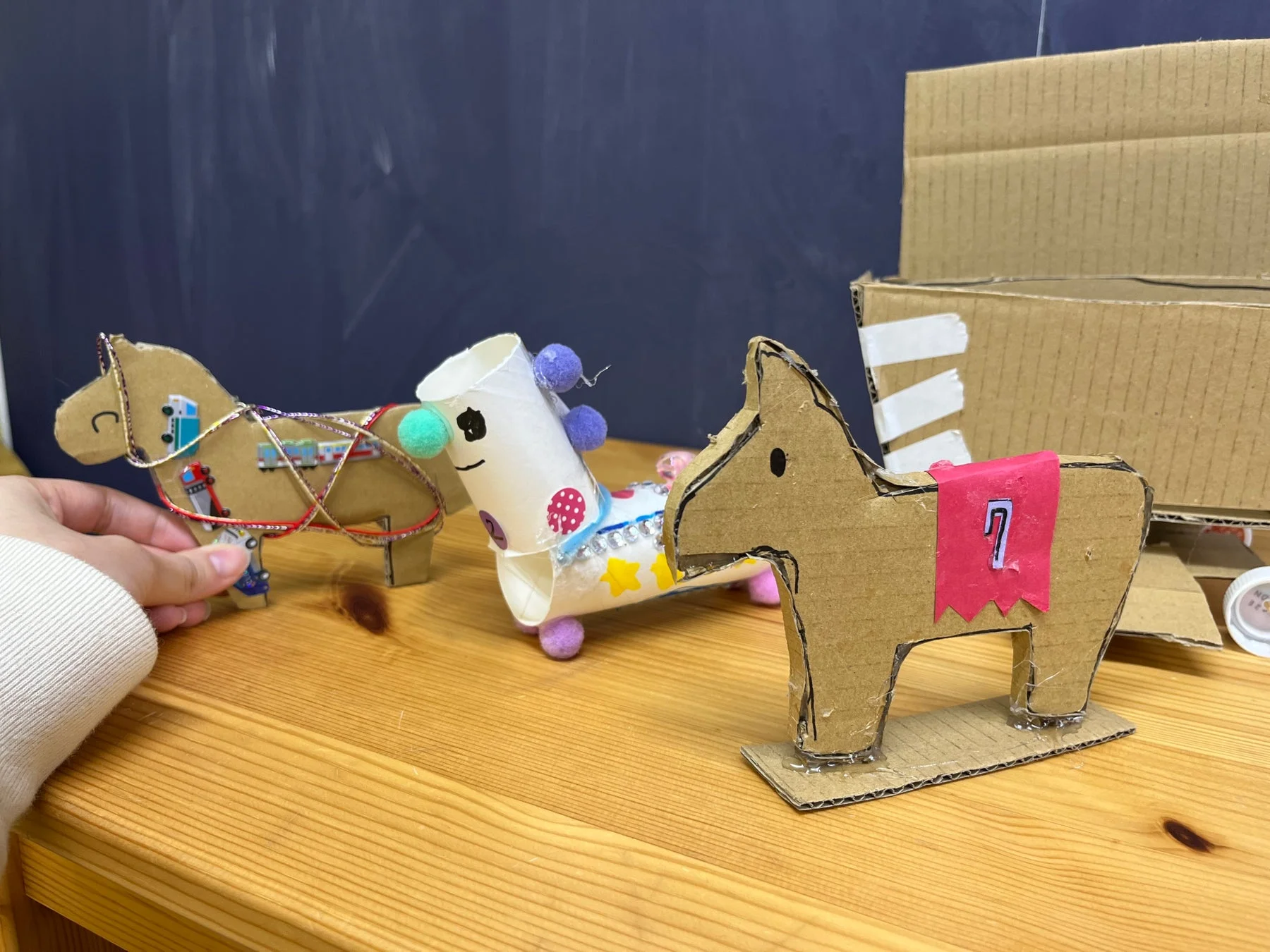 木製のテーブルに並べられた、手作りの段ボール製の馬と紙製のカラフルなユニコーンのようなクラフト作品。