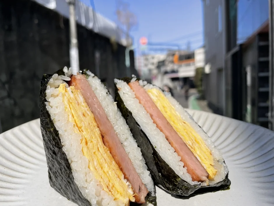 青空の下、白い皿に盛り付けられたスパムおにぎり2個のクローズアップ写真