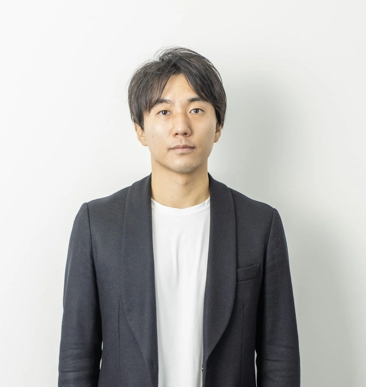 白い背景の前で、黒いジャケットと白いTシャツを着用した若いアジア人男性のポートレート写真