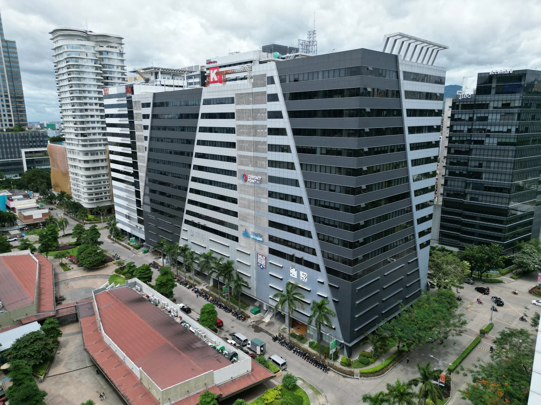 近代的な高層ビルが立ち並ぶ都市景観。特徴的なデザインのビルには「CONTACT POINT 360」や「QQ English」などの企業ロゴが見える。道路には車両が行き交い、ヤシの木が植えられ、活気あるビジネス街の様子が捉えられている。