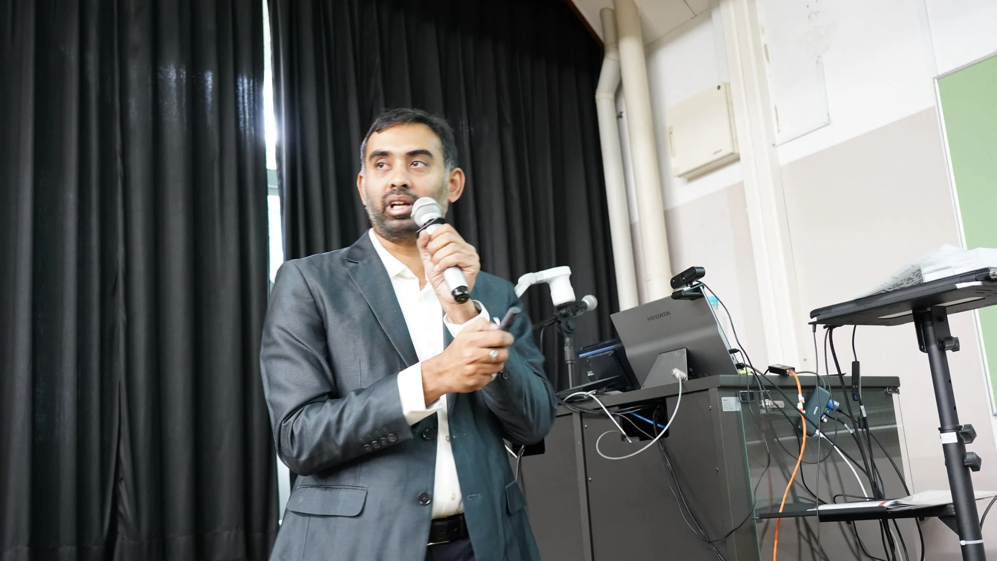 スーツを着た男性がマイクを持って話している様子を捉えた画像です