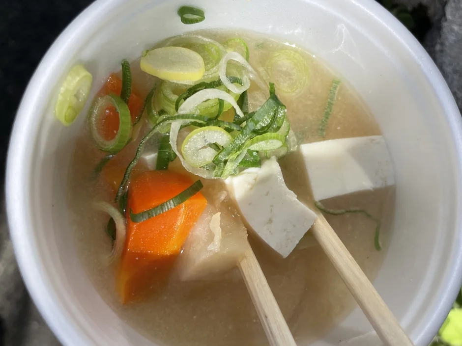 白い器に入った温かい日本の汁物で、豆腐、人参、長ネギが具材として豊富に入っている