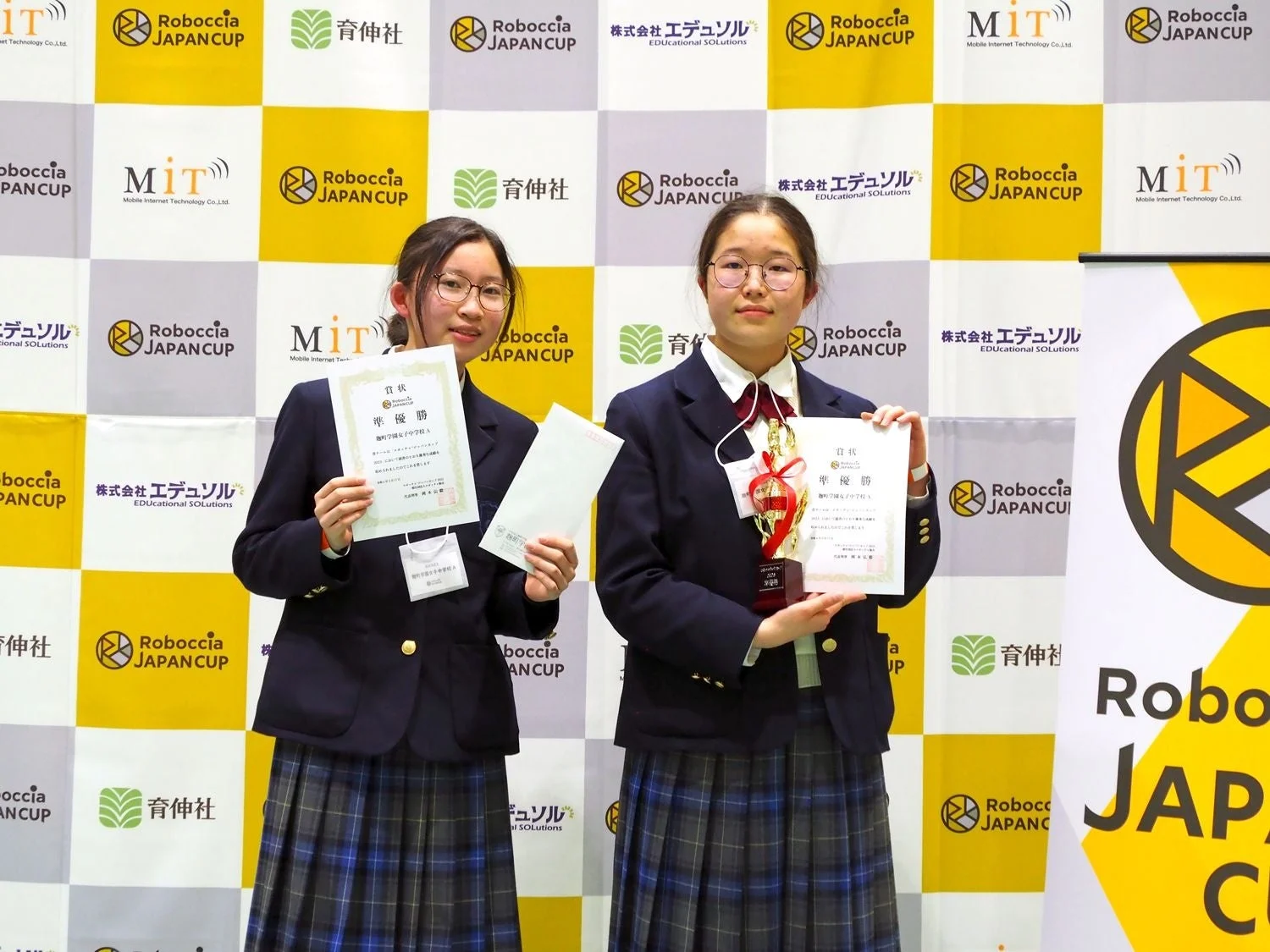 ロボット競技大会で準優勝し賞状とトロフィーを掲げる女子学生2名