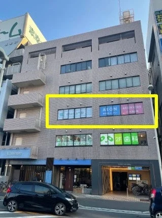 都市部にある複数のテナントが入居する商業ビルを写した画像です。ビルには歯科クリニックやAEONなどの看板が見られ、2階には歯科医院が入っています。