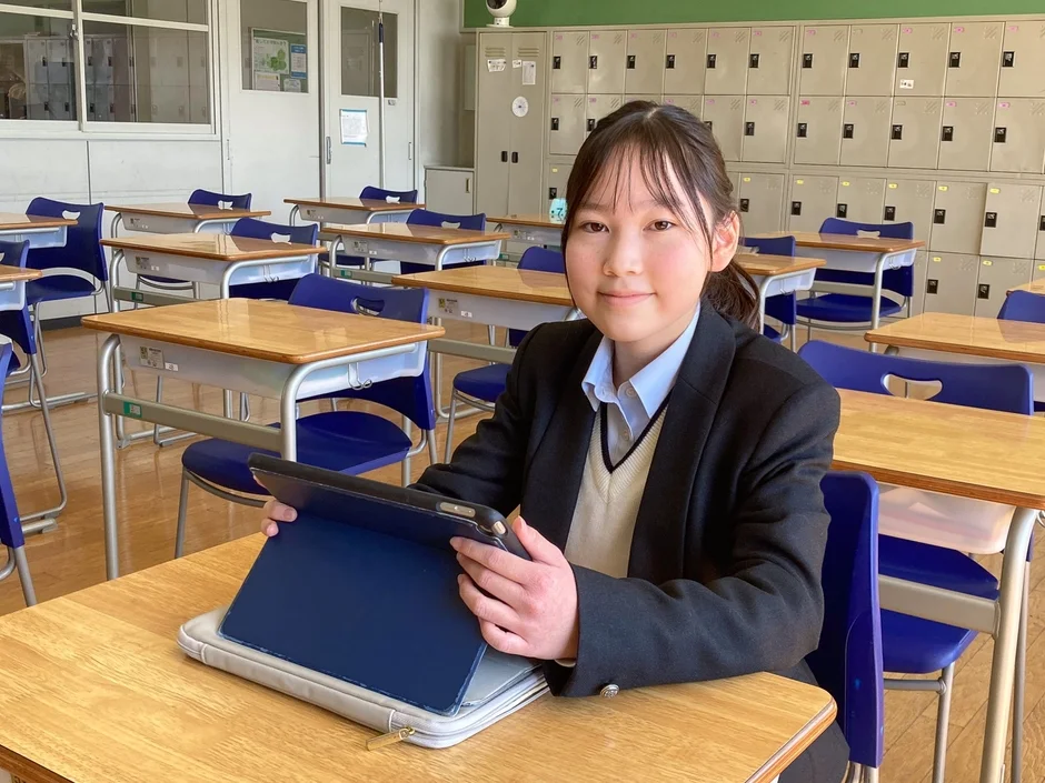 教室で制服姿の女子生徒がタブレットを手に笑顔を見せている