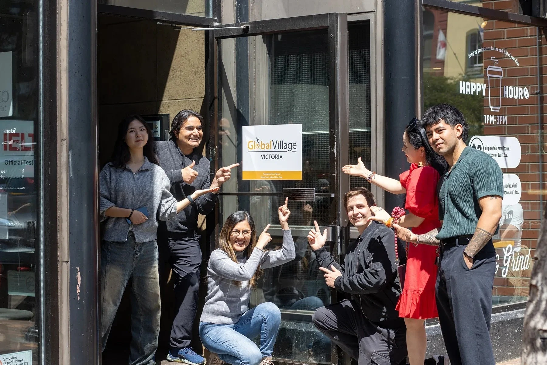 GlobalVillage VICTORIAの看板の前で若者たちが笑顔でポーズをとっている様子