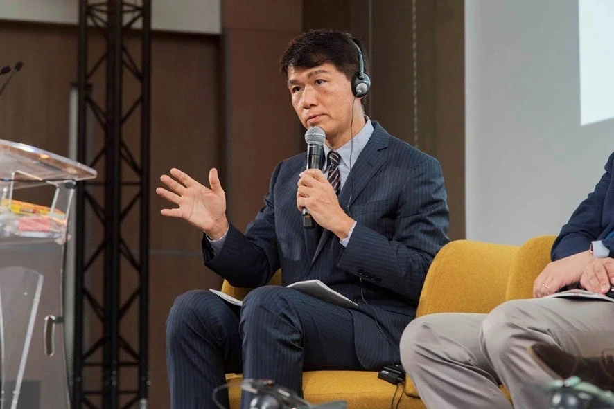 スーツ姿の井上岳久氏がマイクの前で話している様子