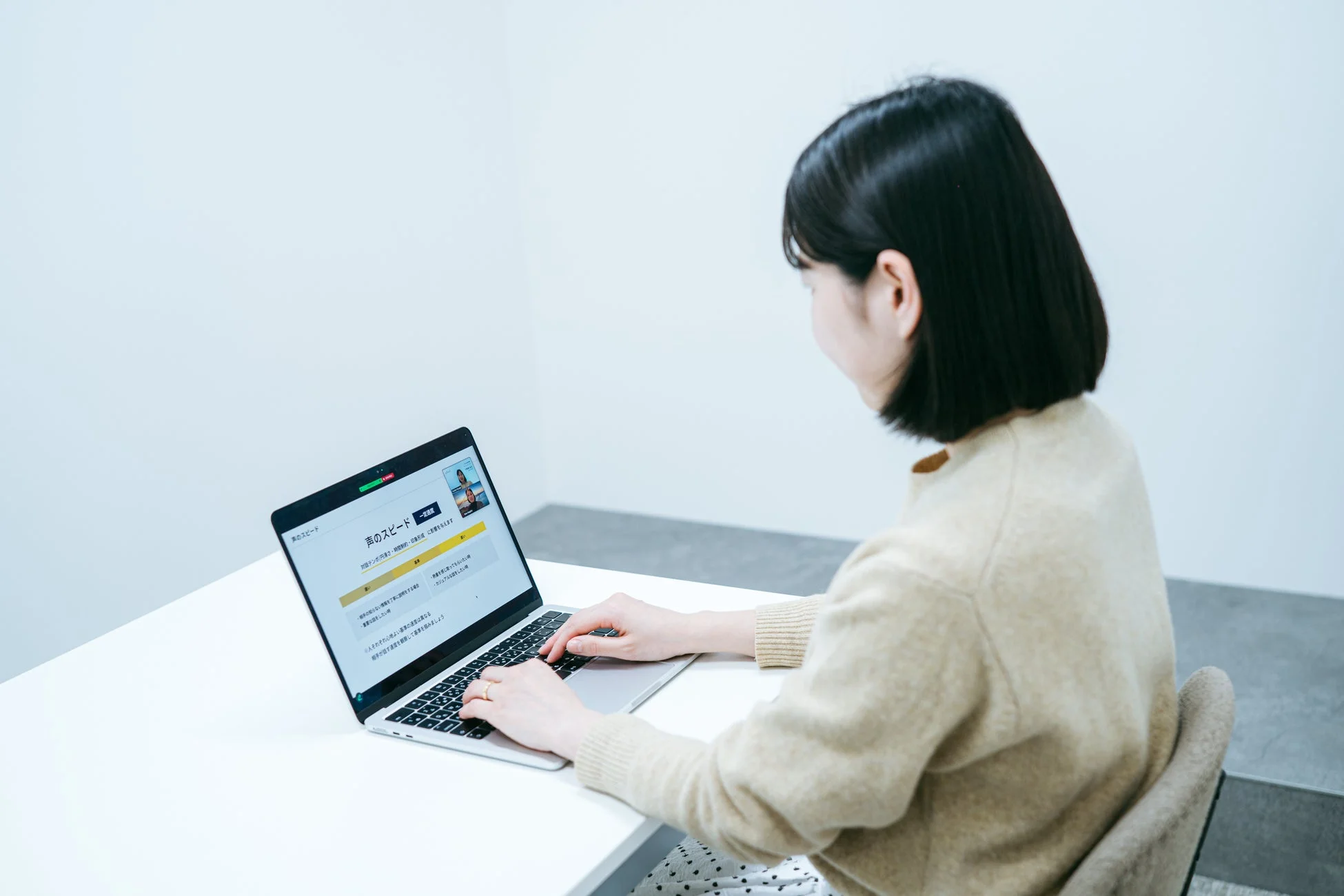 白い机でノートパソコンを操作する女性の後ろ姿