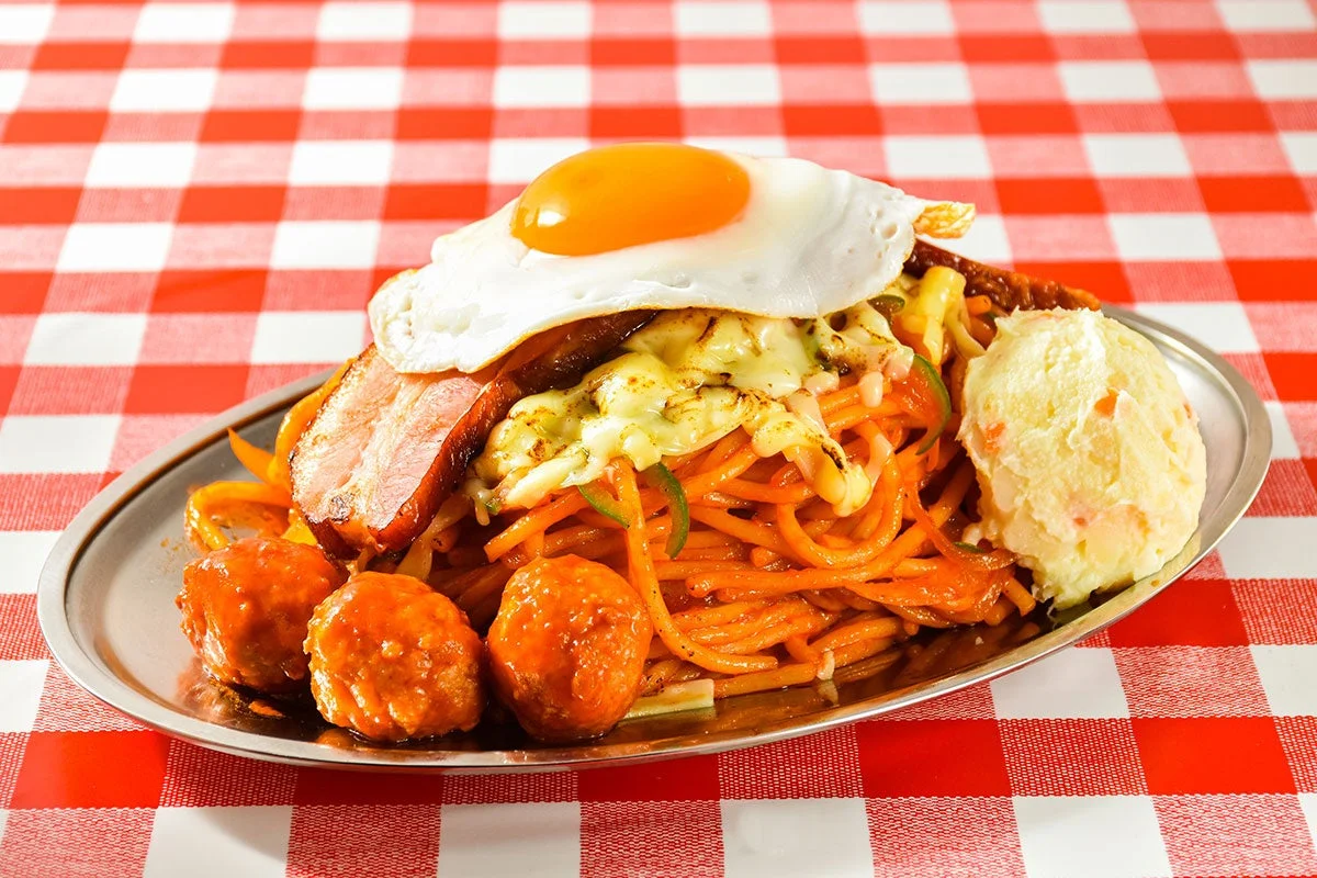 赤と白のチェック柄のテーブルクロスの上に乗せられた、ナポリタンに目玉焼き、ベーコン、ミートボール、ポテトサラダが盛り付けられたボリューム満点の洋食プレートです。