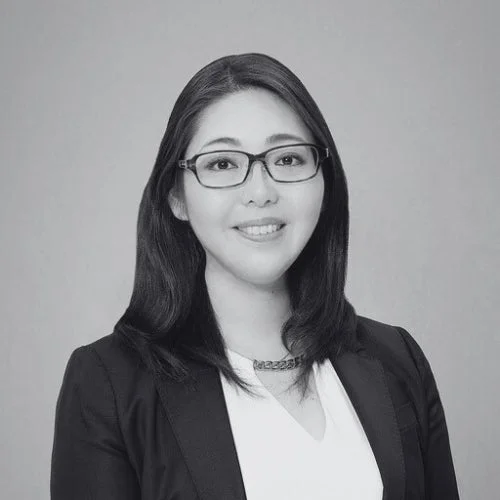 眼鏡をかけたアジア系の女性が、ビジネススタイルの服装で優しく微笑んでいる白黒のポートレート写真