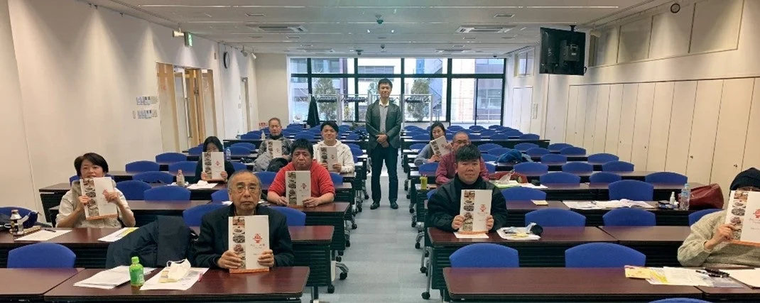 教室のような空間で、複数の参加者が食品のカタログを手に持ち、講師らしき男性が立っているセミナーの様子です。お歳暮に関連する学習会や説明会と推測されます。