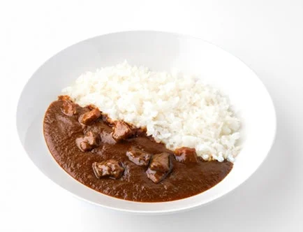 白い皿に盛られたご飯と、深みのある茶色のルーに角切りの肉が入ったカレーライスです。シンプルながらも食欲をそそる一品が白い背景に映えています。