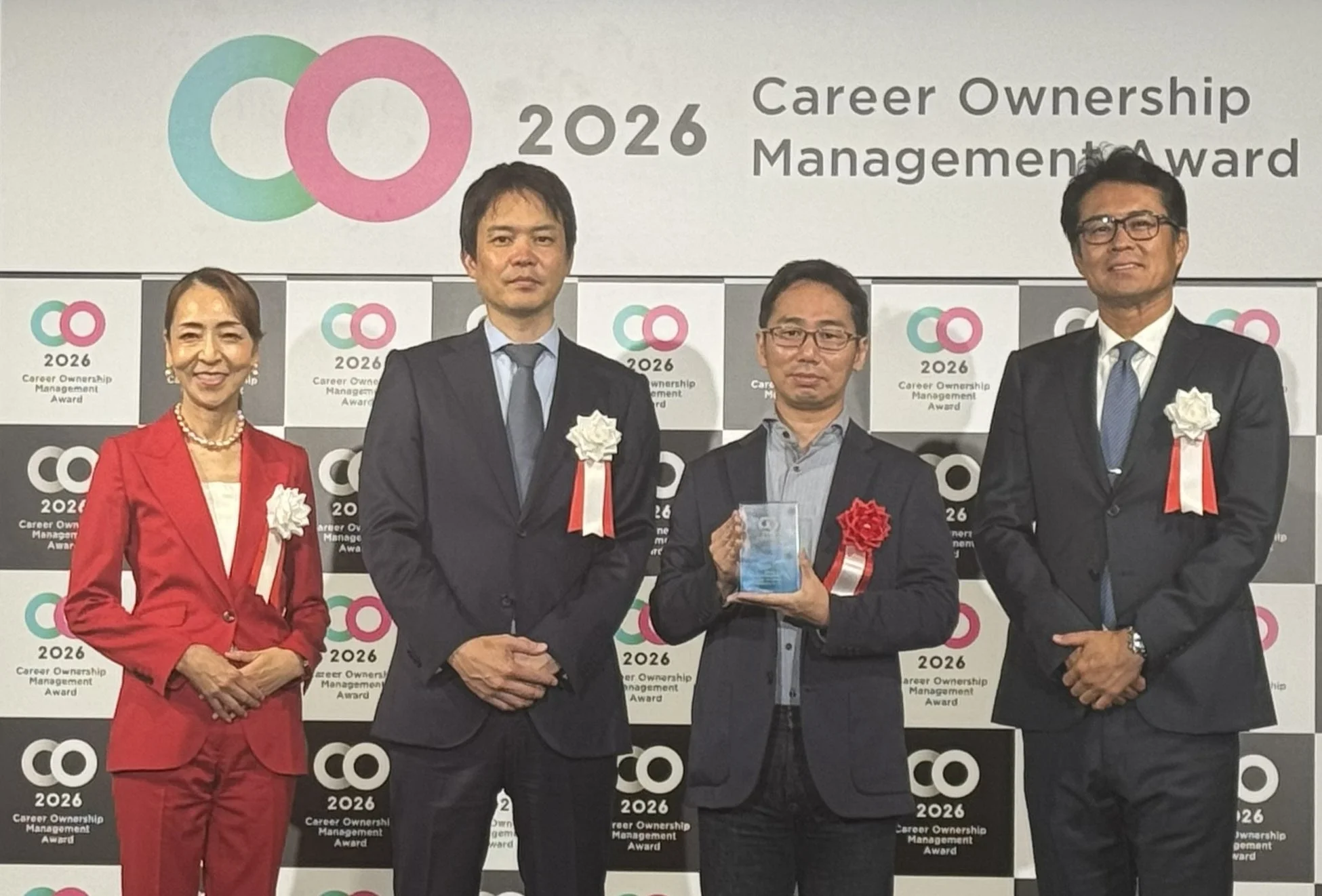 「CO 2026 Career Ownership Management Award」の授賞式で、男女4名が背景のロゴの前で並んで立っています。1名の男性がトロフィーを手にしています。