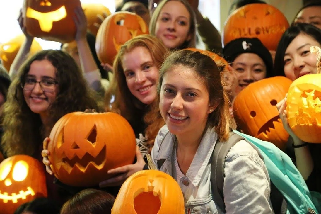 ハロウィンのイベントで、多くの若者たちが笑顔で様々な表情のジャックオーランタンを手にしている様子を捉えた写真です。楽しげな雰囲気が伝わってきます。