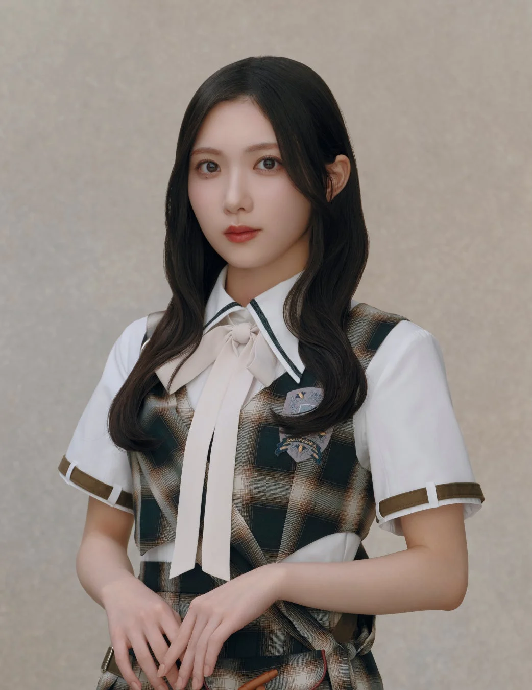 学生服のような衣装を着用した若い女性のポートレート。チェック柄のベストと白いシャツ、大きなリボンが特徴で、カメラをまっすぐ見つめる姿が写っています。