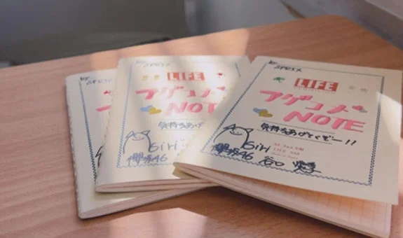 木製の机の上に3冊のノートが置かれている。ノートの表紙には「LIFE」「アブコノス」「NOTE」という文字と、手書きの「Biri」「博多46」という文字、そして可愛らしい猫のようなキャラクターが描かれている。柔らかな光が差し込んでいる。