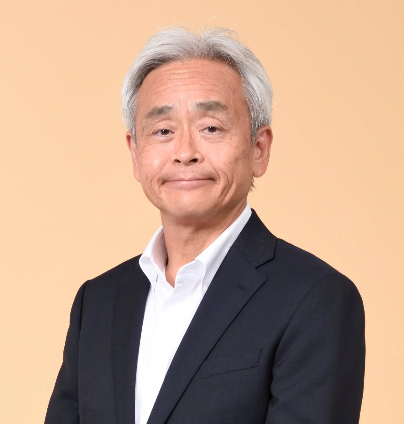 白髪の日本人男性が白いシャツとダークスーツを着用し、穏やかな表情でカメラを見ている上半身のポートレート