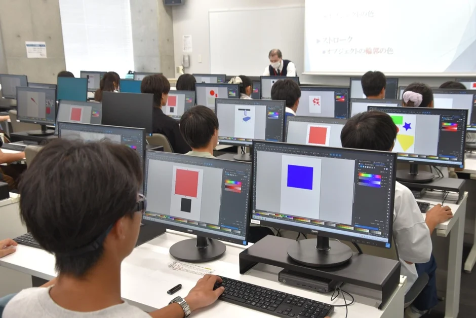 コンピューター室で学生たちがPCを使ってグラフィックデザインの授業を受けている様子