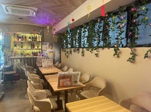 カフェやバーのような店内の様子です。複数のテーブル席とカウンターがあり、壁には植物の装飾が施され、おしゃれで落ち着いた雰囲気の空間が広がっています。