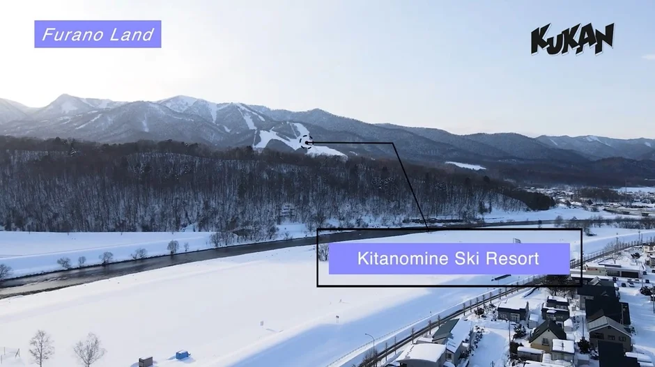 雪に覆われた山々、川、そして北の峰スキーリゾートが見える冬の富良野の広大な風景。上部には「Furano Land」と「KUKAN」の文字も確認できる。