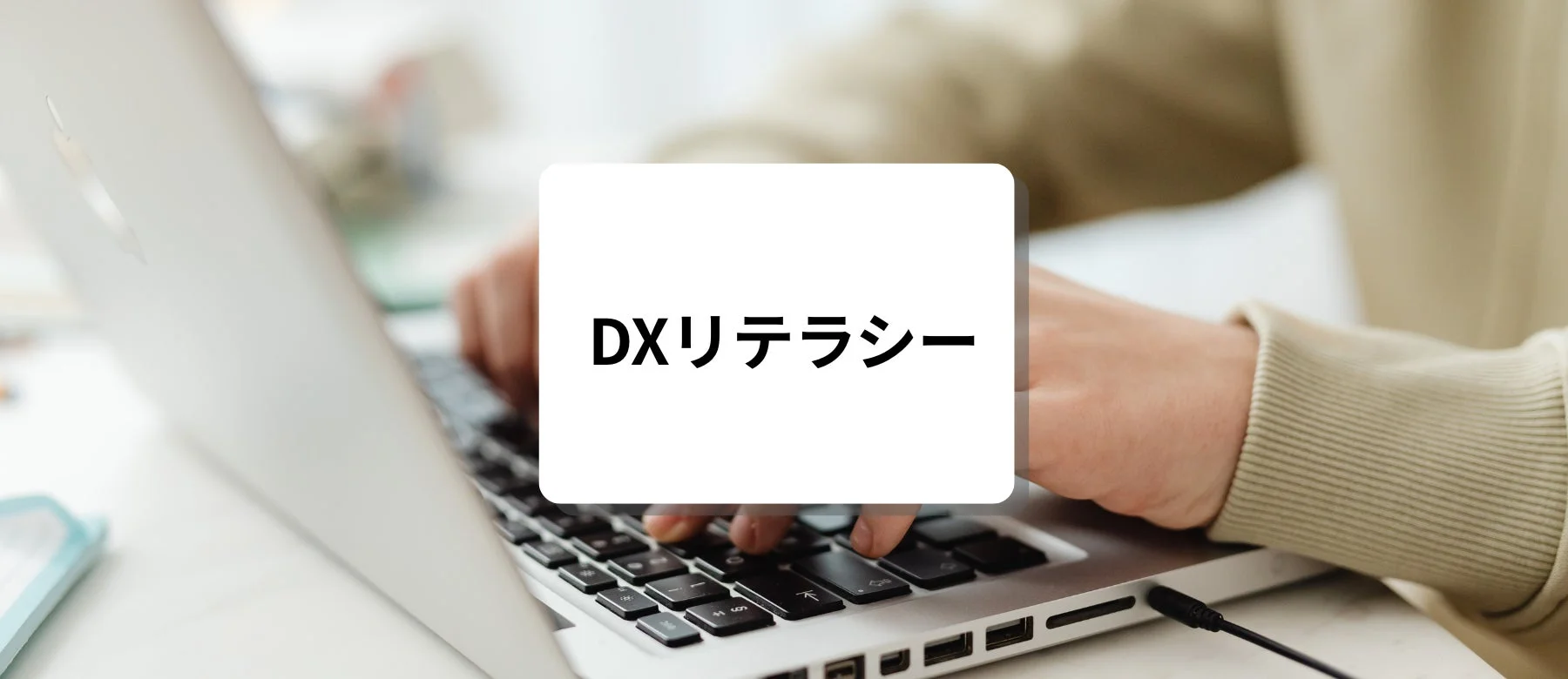 ノートパソコンを操作する人物の手元が写っており、中央に「DXリテラシー」という文字が示されています。デジタルスキルや学習の重要性を示唆する画像です。