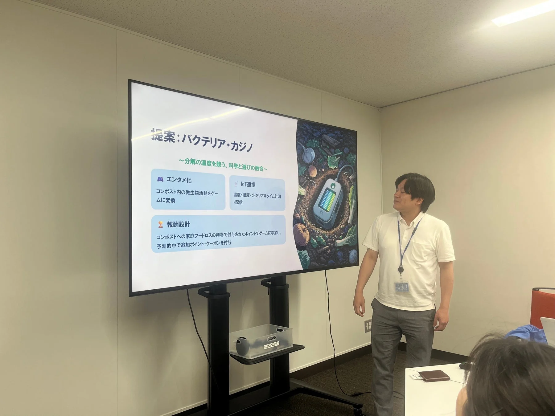 会議室で男性がプレゼンテーションを行っており、スクリーンには「バクテリア・カジノ」と題された提案