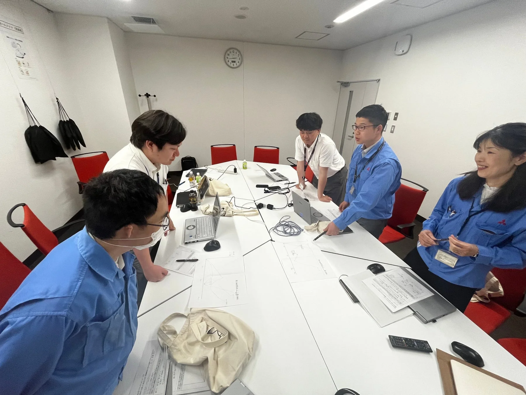 会議室で数人の社員がテーブルを囲み、ノートパソコンや資料を使って活発に議論している様子