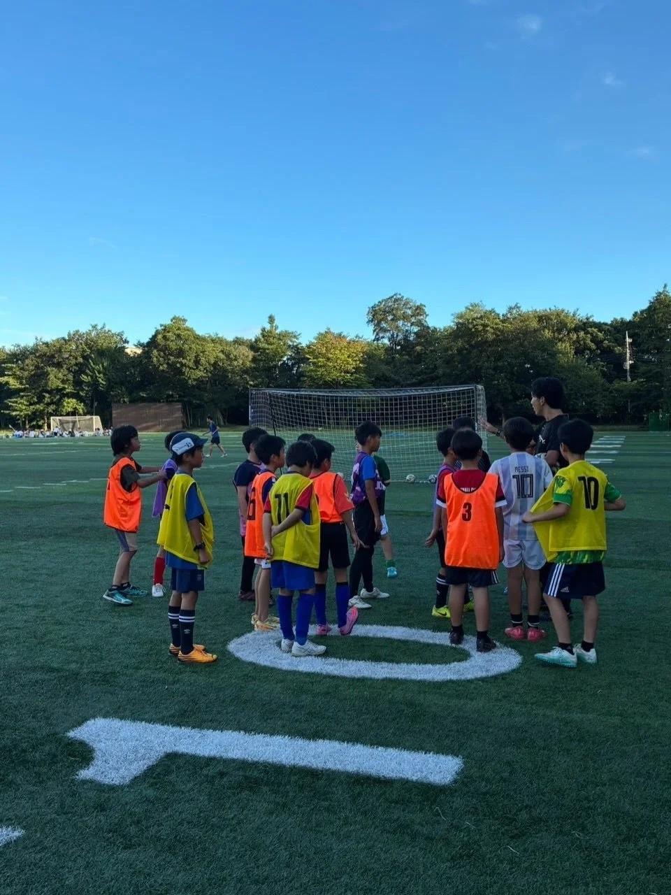 サッカーフィールドでコーチから指導を受ける子どもたち