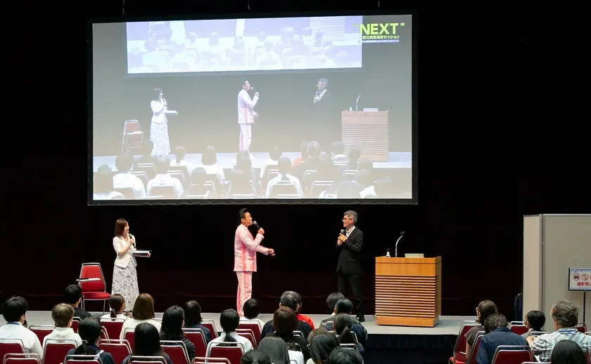ステージ上で3人の登壇者がマイクを持ち、聴衆に向けて話しています。背後のスクリーンには「NEXT」と「国立公園セッション」の文字が表示されており、講演会またはセミナーが開催されている様子です。